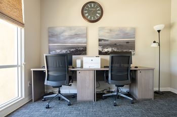 Two computers on a desk in a room with a clock on the wall.